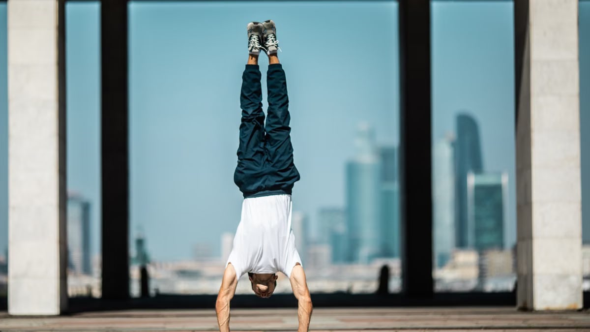 Man performing a handstand outdoors with a cityscape backdrop, embodying strength and balance.